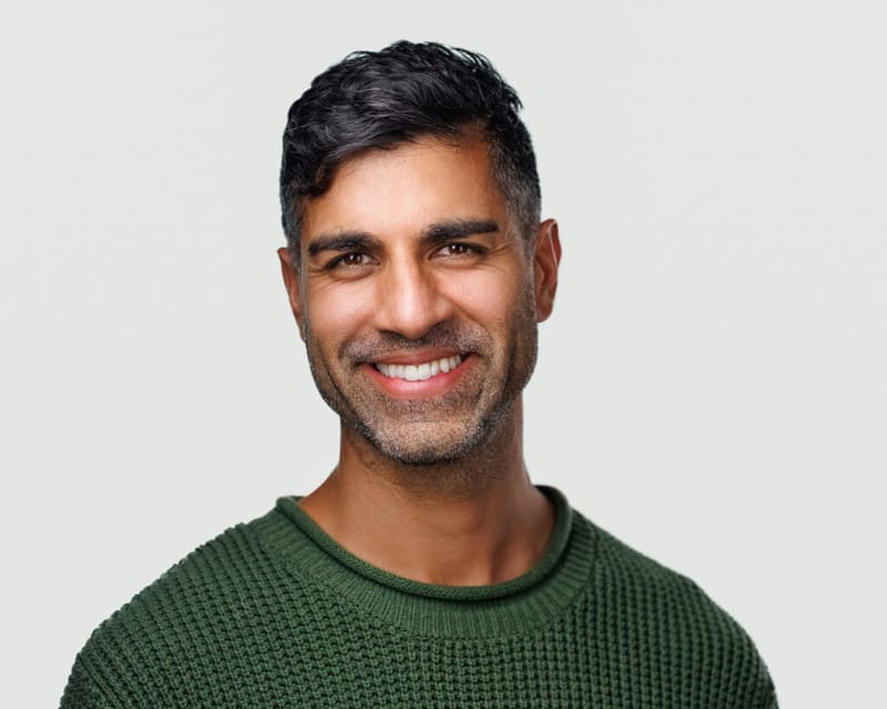 Khurram Naik smiling in a green sweater against a light grey background