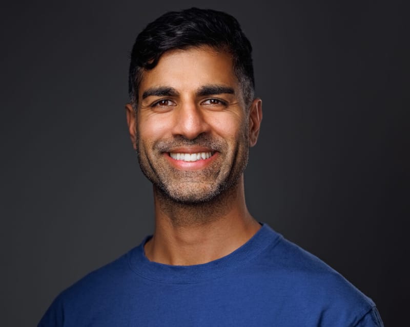 Khurram Naik smiling in a blue shirt against a dark grey background